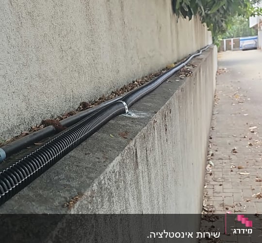 התקנת צנרת מים חיצונית עם חבקים לאורך חומת בטון בגינה
